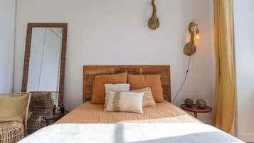 Ein Schlafzimmer mit Holz-Kopfteil, einem großen Spiegel, einem Bett mit vielen Kissen, einer Wandleuchte und einem kleinen Tisch mit Dekoration.