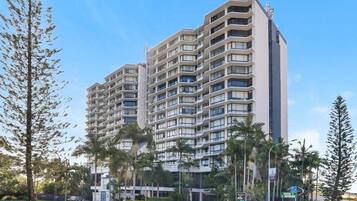 Un edifici residencial de diversos pisos amb balcons, envoltat de palmeres i un cel clar.