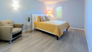 Een slaapkamer met een bed, een stoel, een nachtkastje en een raam.