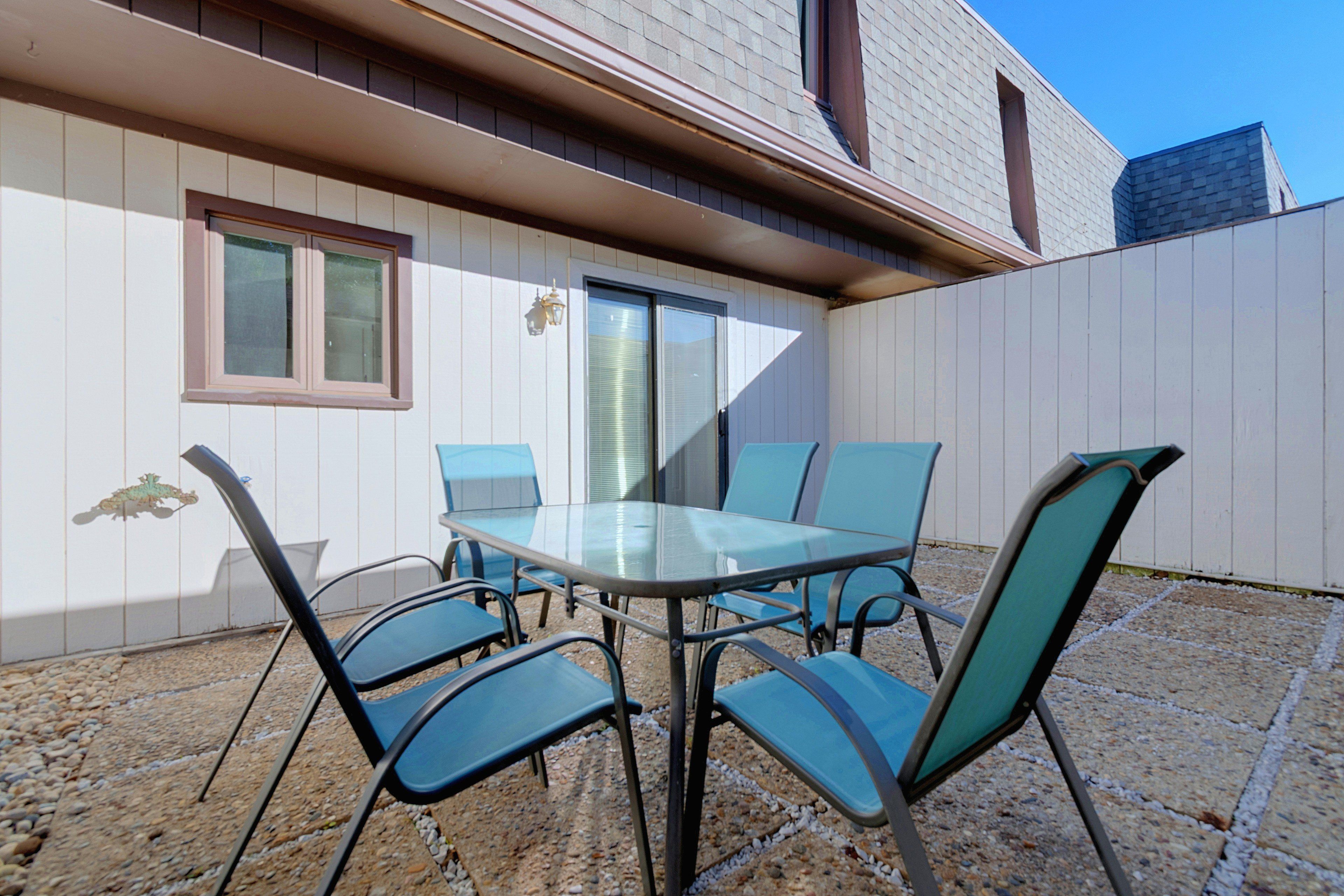 Een terras buiten met een glazen tafel en vier stoelen, een raam en een deur.