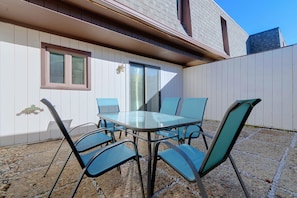 Een terras buiten met een glazen tafel en vier stoelen, een raam en een deur.