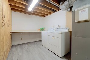 Een wasserette met houten plafond, een wasmachine, een droger en een aanrecht.