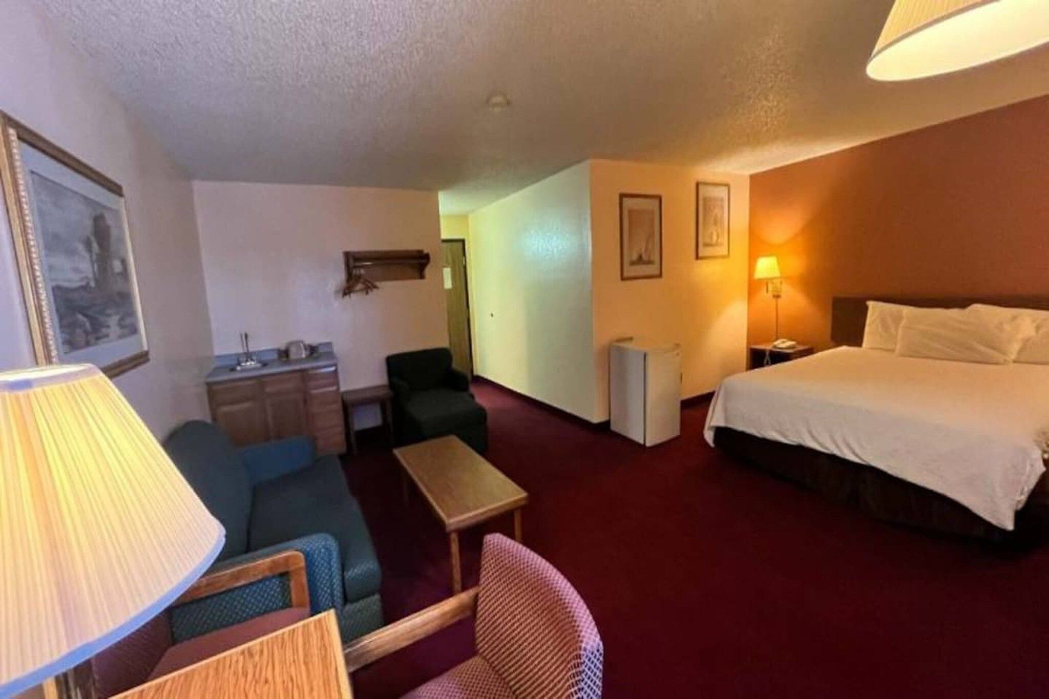 Quarto de hotel com cama, escrivaninha, cadeira, luminária e mesa pequena.