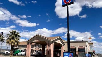 A motel with a large '6' sign, a covered entrance, and a parking area with a van.