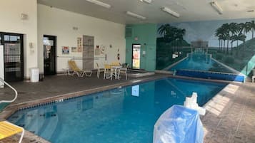 An indoor swimming pool with a mural of palm trees on the wall, a covered area with chairs, and a door marked 'EXIT'.