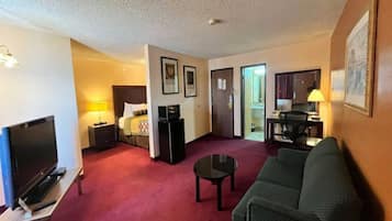 A hotel room with a television, a sofa, a desk with a lamp, a bed, and a door leading to another room.