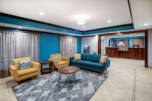 Um hall de hotel com uma mesa de recepção, um sofá azul, duas poltronas e uma mesa de centro.