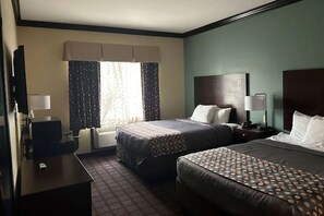 Habitación de hotel con dos camas, un escritorio, una silla, un televisor y una ventana con cortinas.