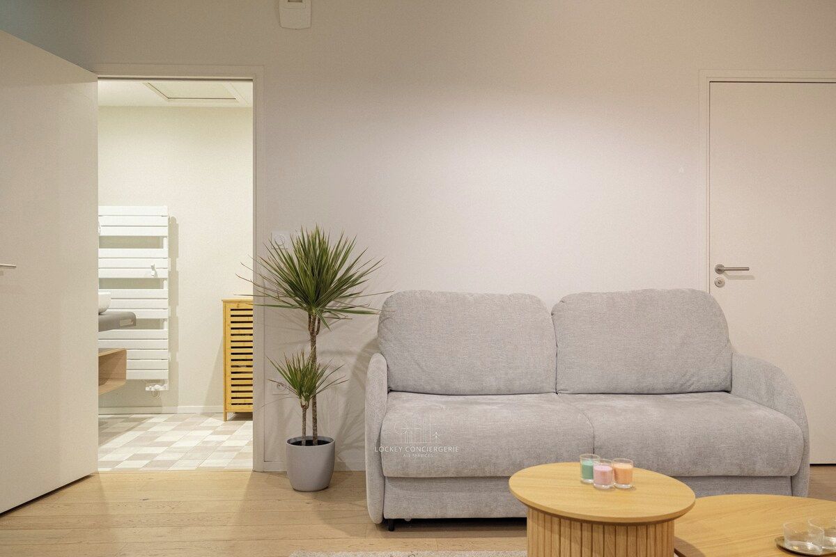 A modern living room with a grey sofa, a round wooden coffee table, a potted plant, and a door to another room.