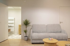 A modern living room with a grey sofa, a round wooden coffee table, a potted plant, and a door to another room. - Joli studio spacieux en hypercentre (La Rochelle)