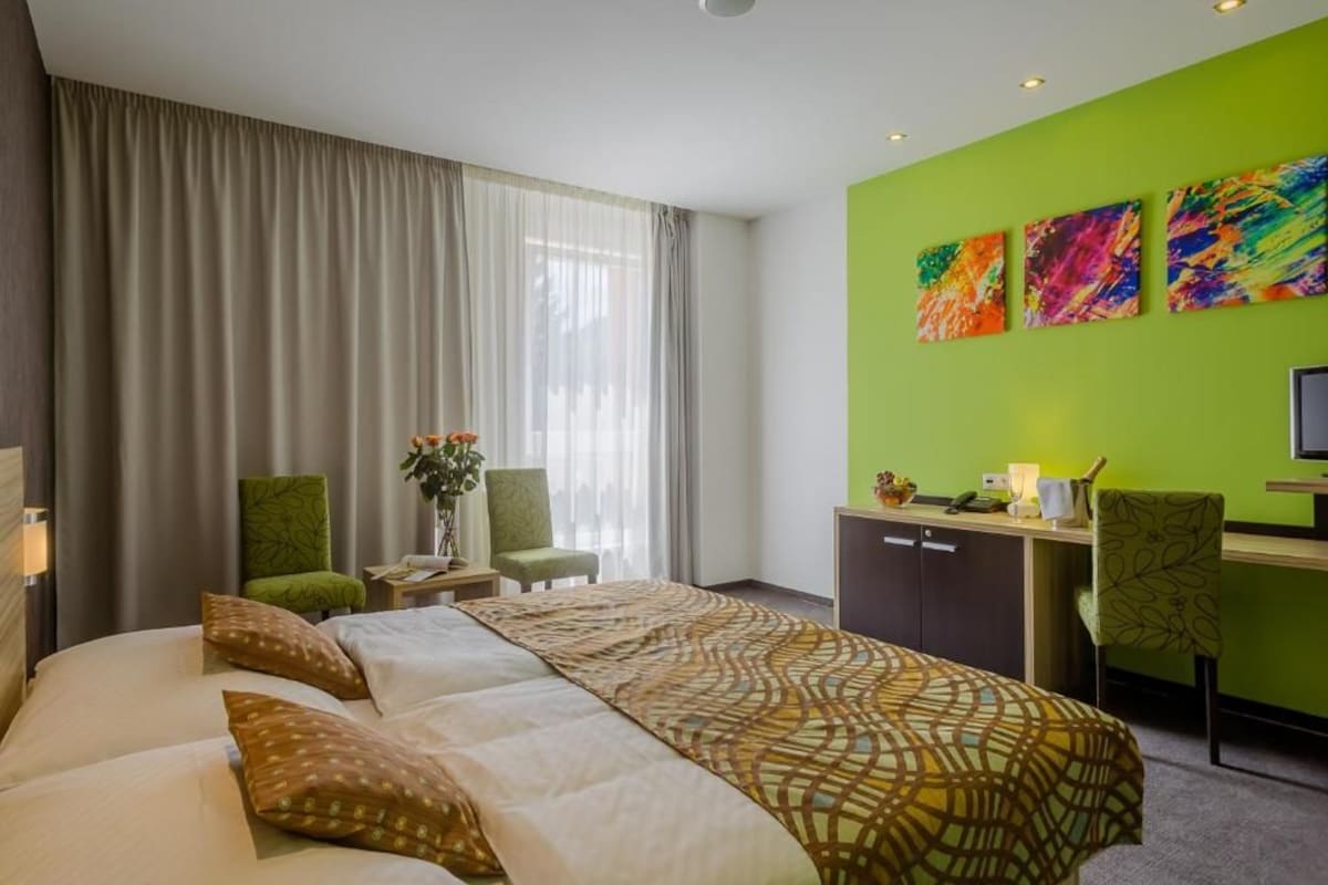 A hotel room with a large bed, a desk, and a green accent wall.
