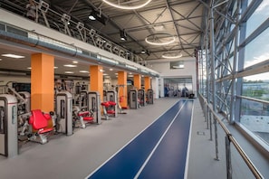 A gym with exercise equipment, a blue running track, and large windows. - Hotel TENIS (Zvolen)