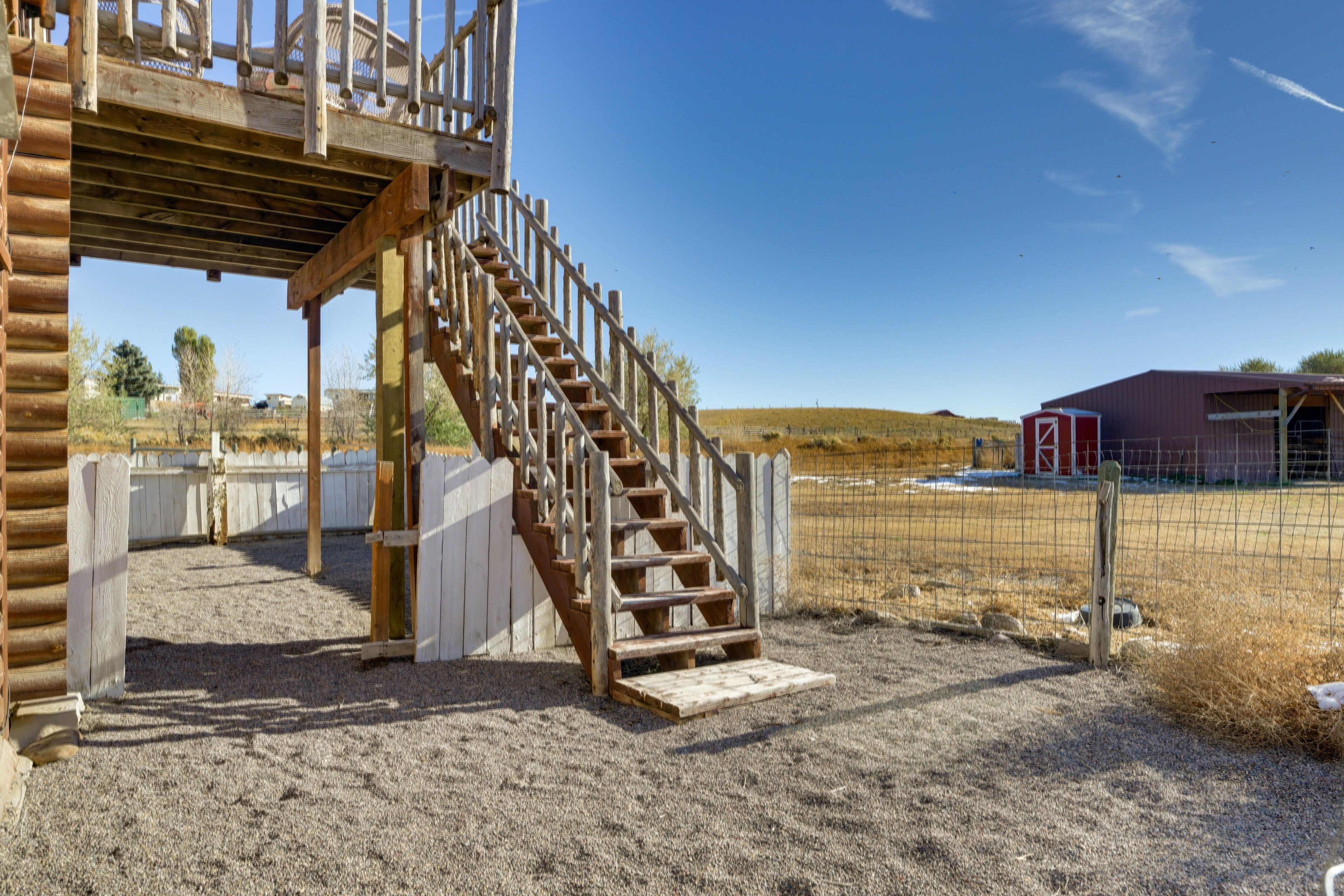 A wooden staircase leading to a covered area with a view of a red barn and open field.