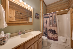 Un baño con tocador de madera, un espejo con luces, un lavamanos, un inodoro y una cortina de ducha con estampados de animales.