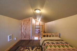 Une chambre avec une porte en bois, un lit recouvert d’une couverture à motifs, un radiateur et un couloir menant à une autre pièce.