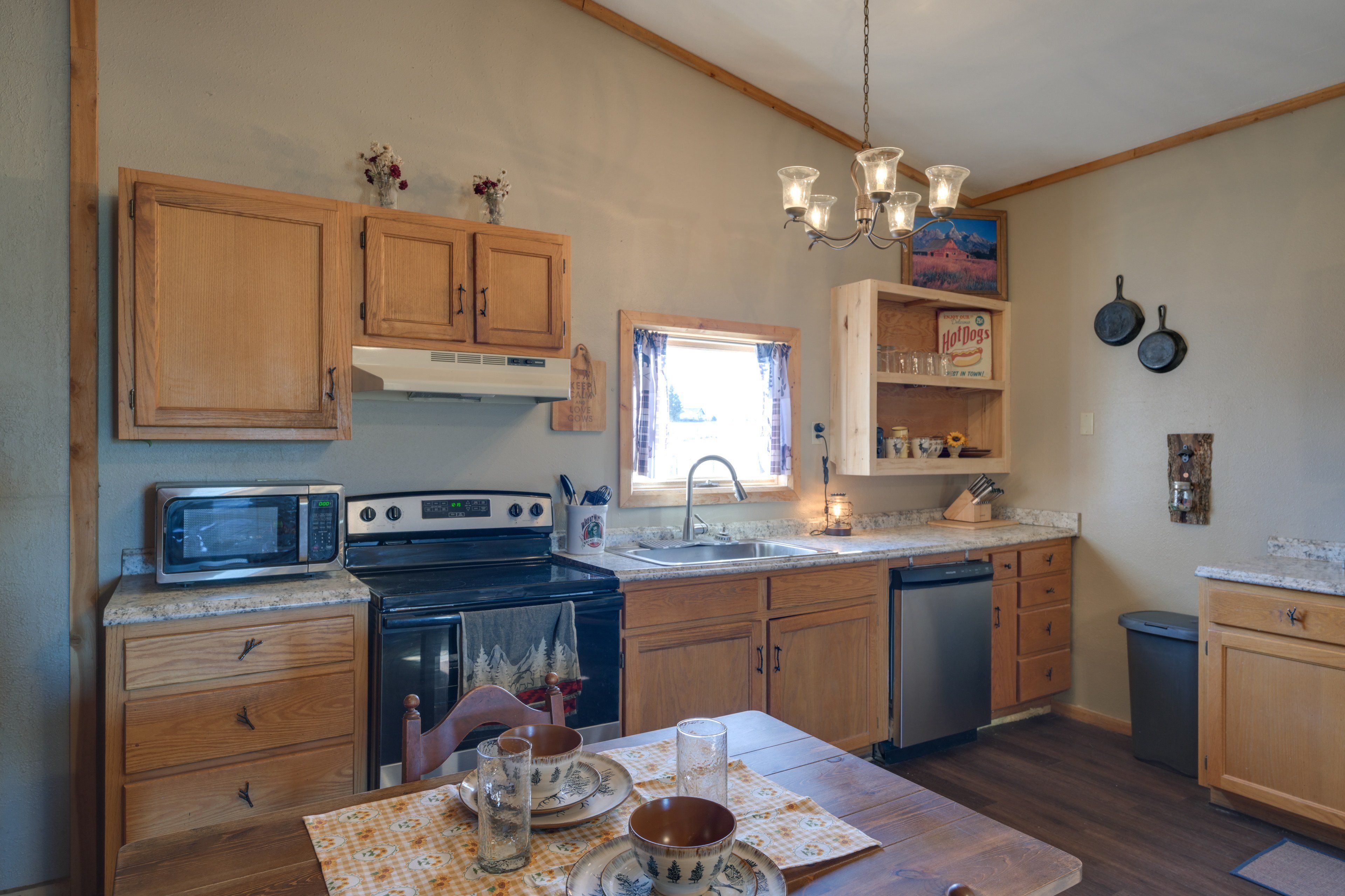 A kitchen with wooden cabinets, a microwave, stove, sink, and a dining table set with plates and a glass.