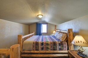 Un dormitorio con estructura de cama de madera, colcha con motivos de animales, mesita de noche con lámpara y ventana con cortinas.