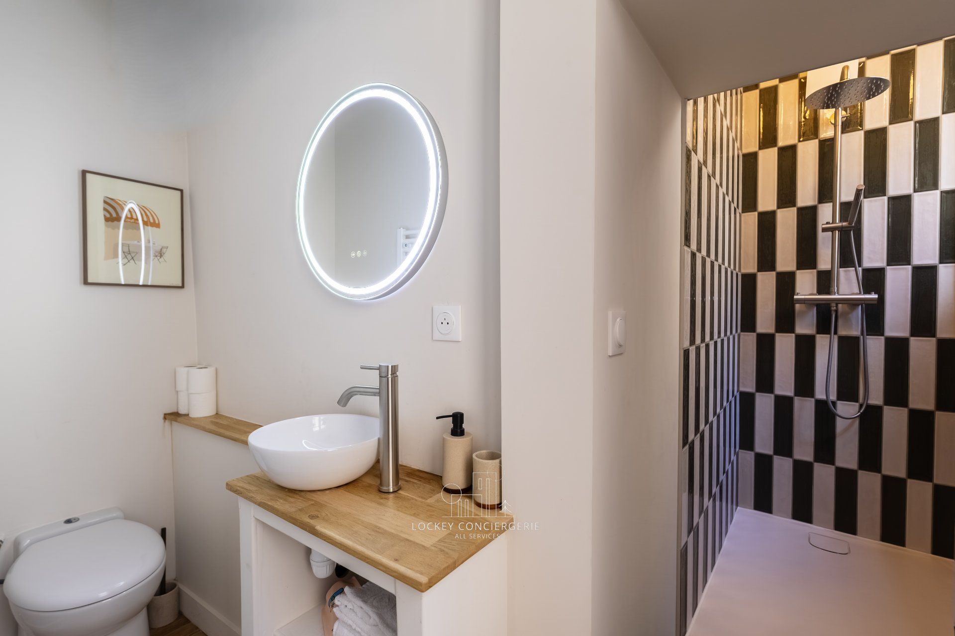 A modern bathroom with a round mirror, a white sink, and a black and white checkered shower wall.
