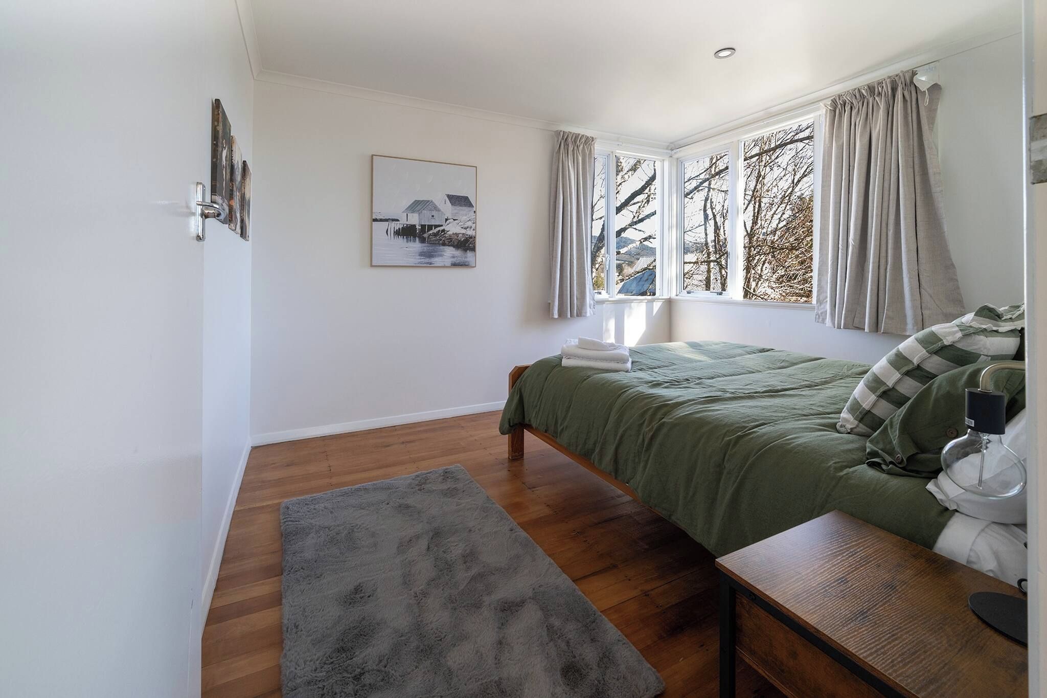 Une chambre à coucher avec un lit, une table de chevet, une lampe, un tapis et un tableau au mur.