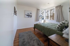 A bedroom with a bed, a bedside table, a lamp, a rug, and a painting on the wall. - The Jumping Trout Rustic Hideaway (Tūrangi)