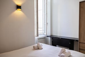 Una camera d'albergo con un letto, un comodino, una finestra e una lampada a parete.