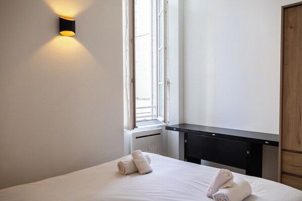 Habitació d'hotel amb un llit, una taula de nit, una finestra i un llum penjant a la paret.