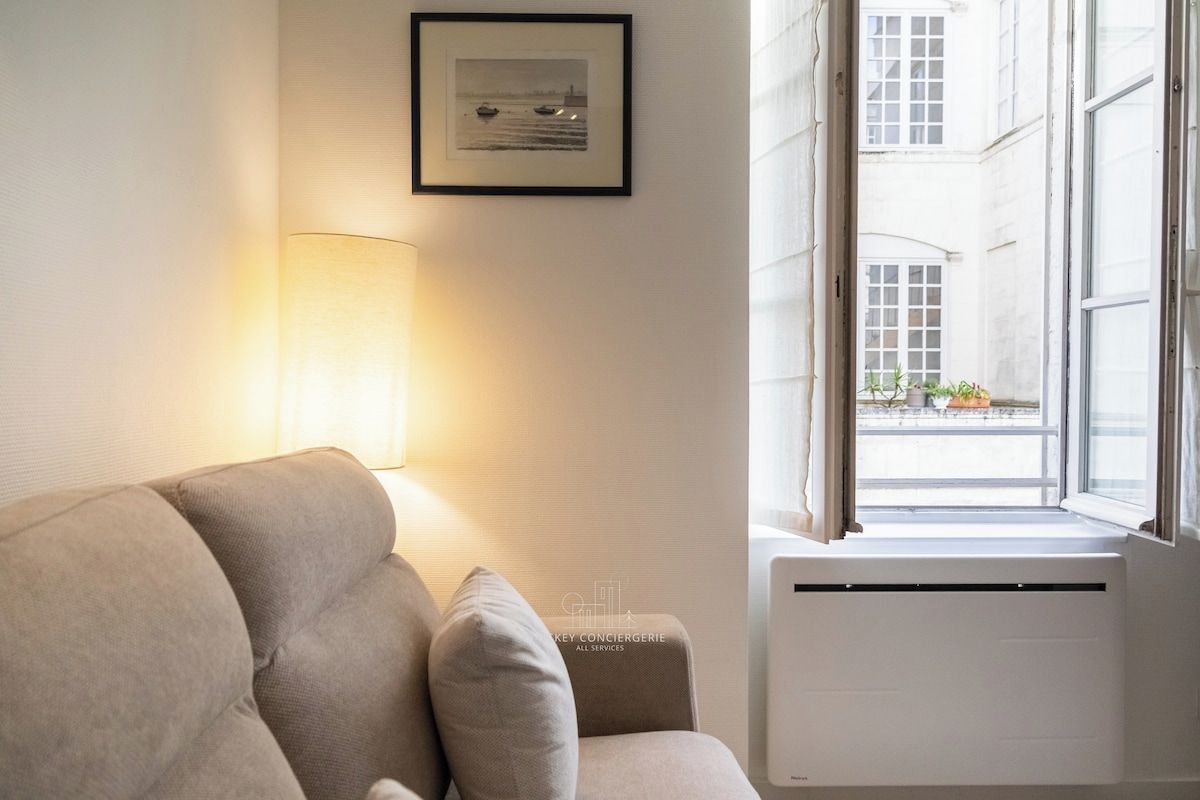 Una habitación con sofá, lámpara, radiador y ventana con vista a edificios.