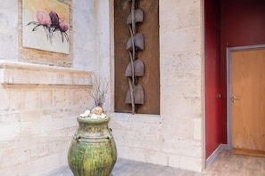 Un muro in pietra con un dipinto di fiori, una scultura in metallo rustico e un vaso verde con pietre.