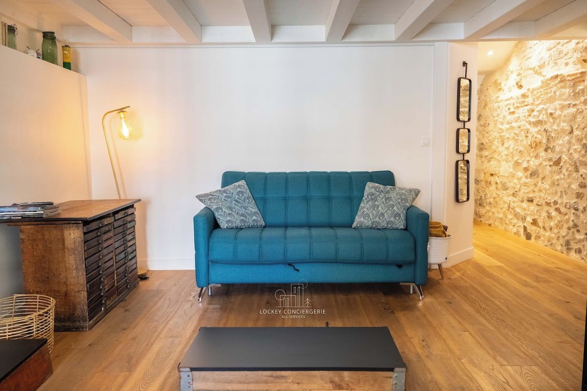 Een smaragdgroene bank met gestreepte kussens, een houten bankje, een wandlamp en een stenen muur.