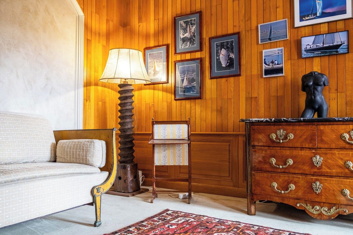 A room with a wooden paneled wall, a sofa, a lamp, a dresser with drawers, and framed pictures.