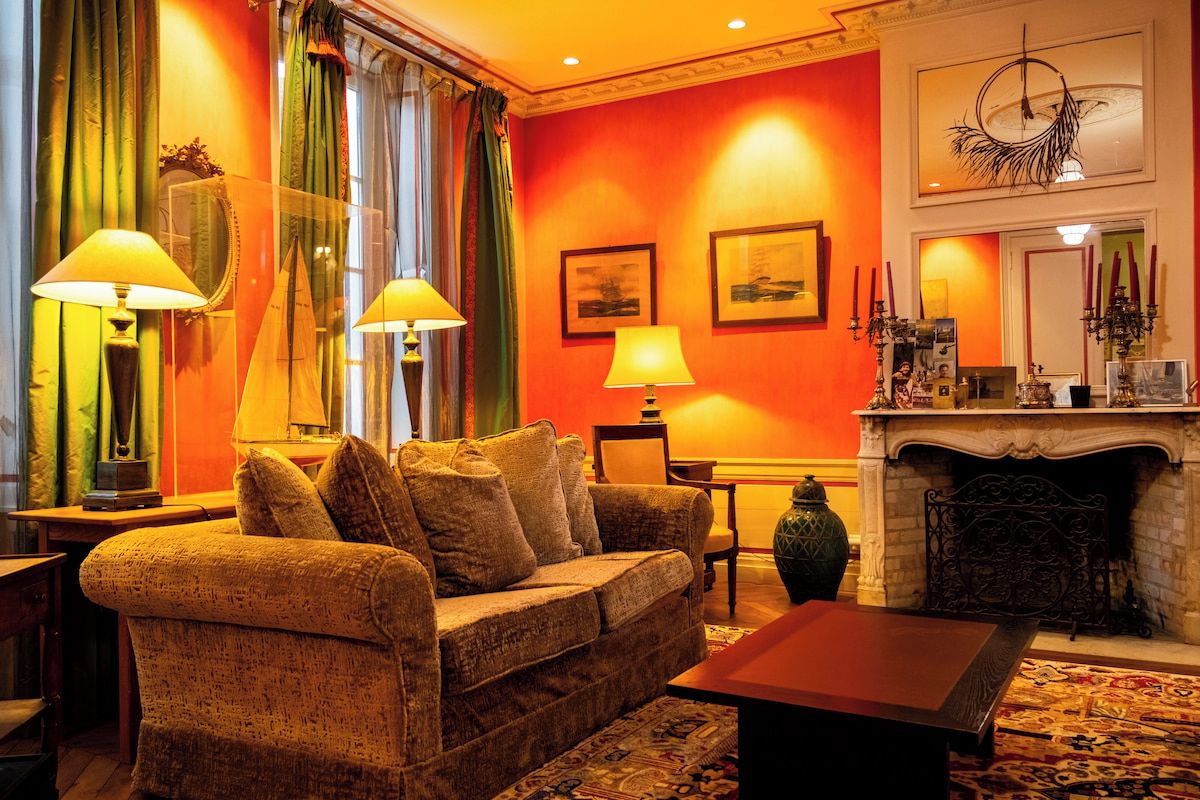 A warmly lit living room with a sofa, lamps, a fireplace, and framed artwork on the walls.