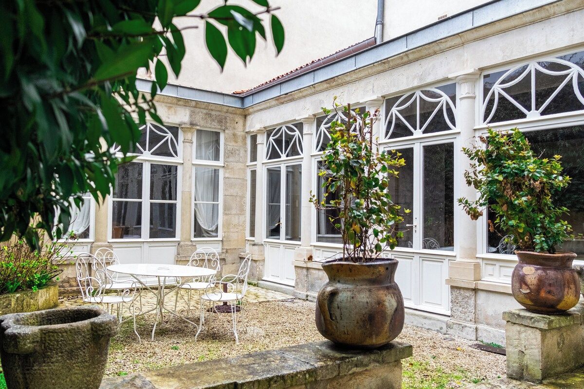 A courtyard with a table and chairs, surrounded by large windows with decorative frames.
