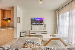 Ett modernt vardagsrum med en platt-TV, en soffa, ett soffbord och en köksdel med träskåp och en inbyggd spis.