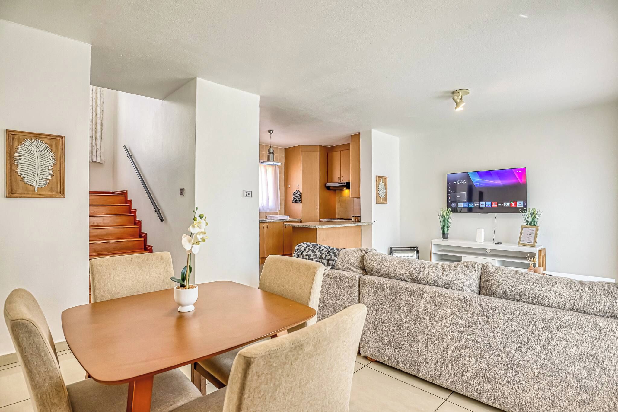 A modern living room with a dining area, a sofa, a TV, and a staircase.