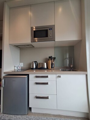 A compact kitchen with a built-in microwave, a small refrigerator, and a countertop with a kettle, toaster, and utensils. - Sandton Studio with Views, Pool, Gym & Parking (Sandton)