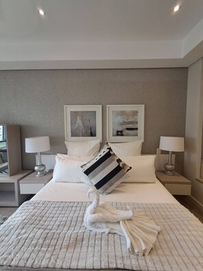 Hotellihuone, jossa on suuri sänky, kaksi yöpöytää, kaksi lamppua ja kaksi kehystettyä kuvaa seinällä.