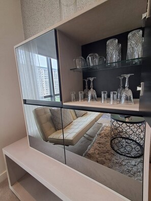 A modern living room with a glass partition, a sofa, and a glass shelf with decorative items. - Sandton Studio with Views, Pool, Gym & Parking (Sandton)