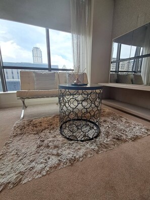 A room with a round table, a sofa, and a view of buildings through large windows. - Sandton Studio with Views, Pool, Gym & Parking (Sandton)