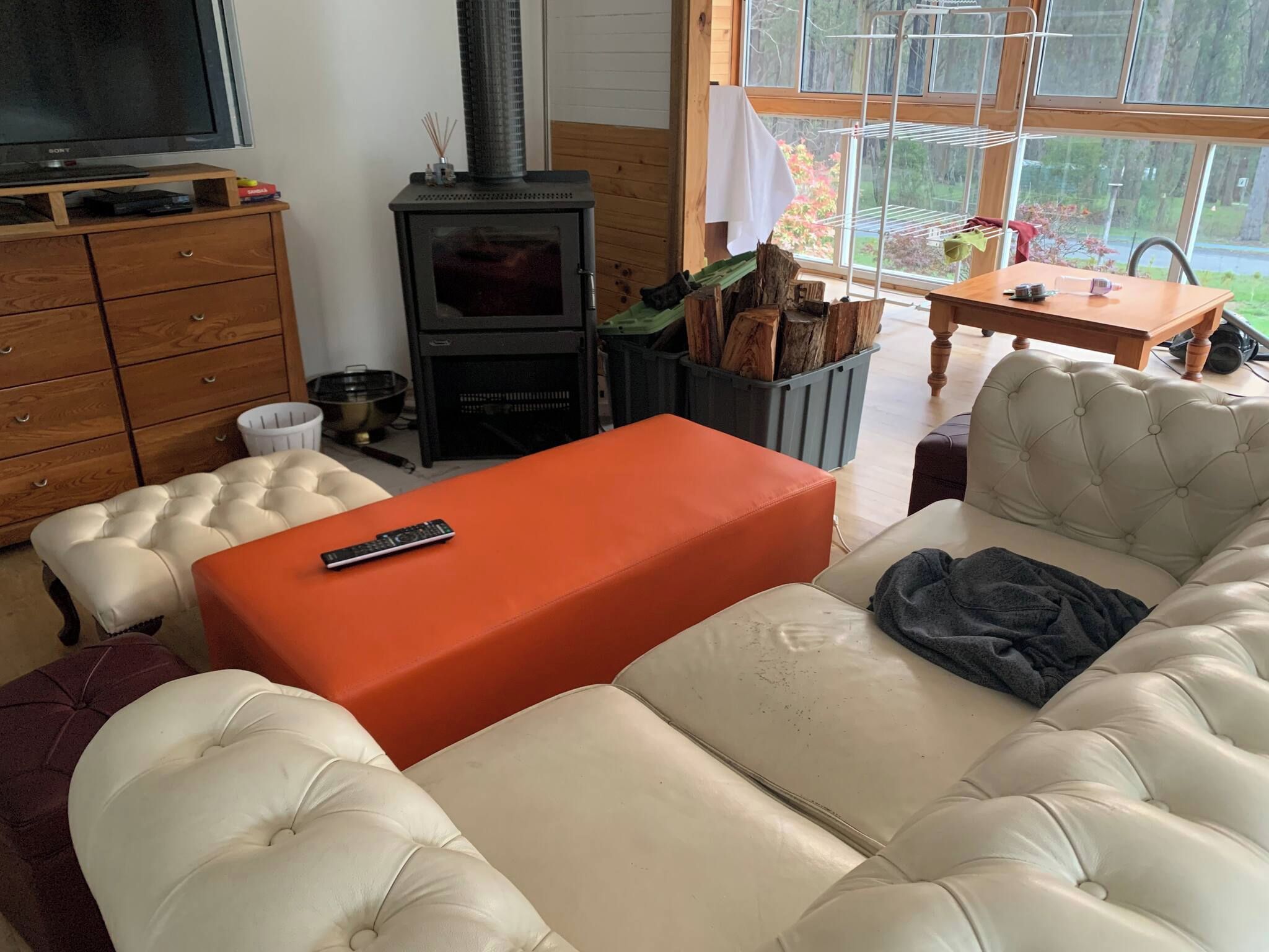 Un salon confortable avec un canapé, un pouf et un téléviseur posé sur un meuble en bois.