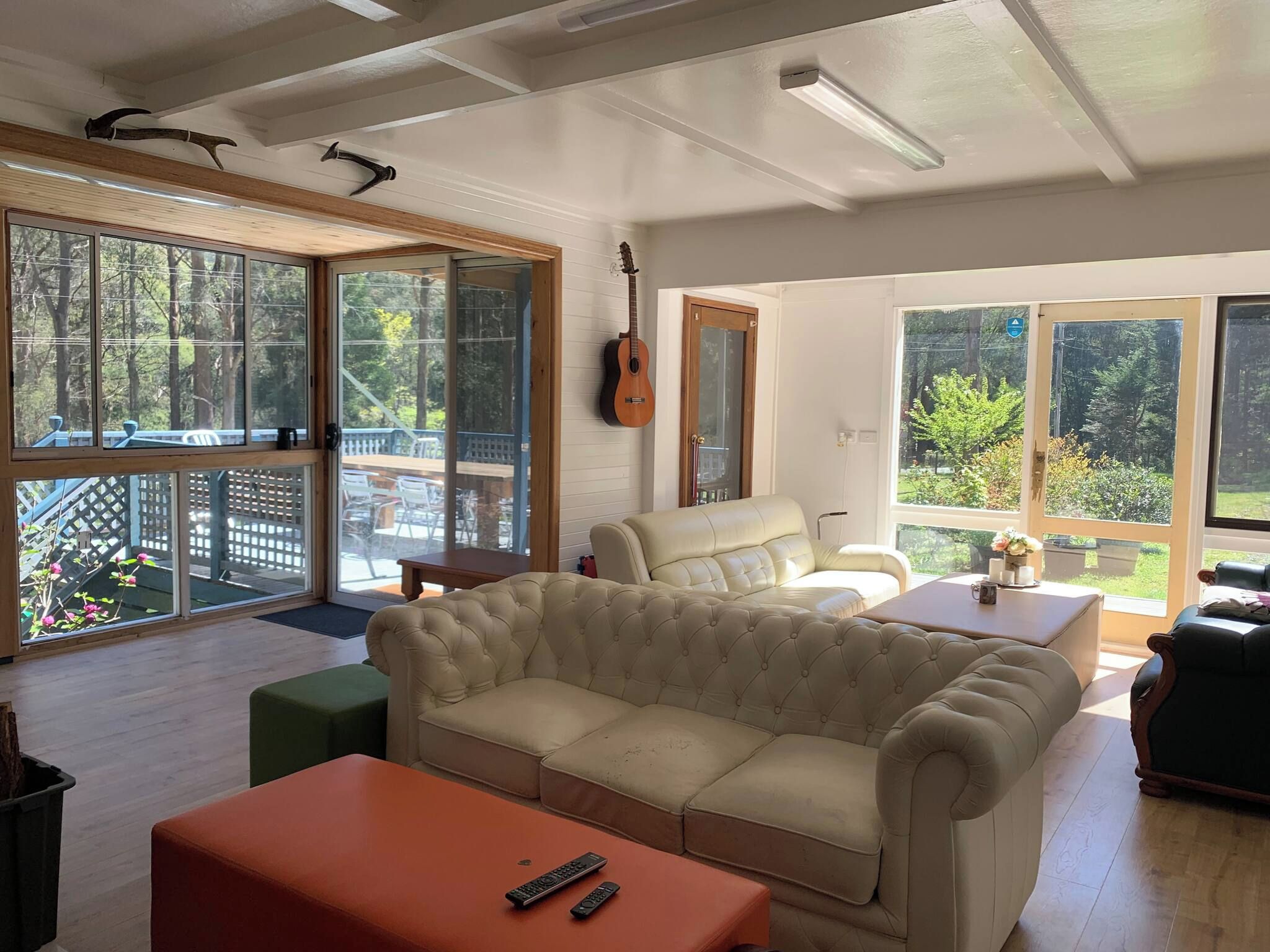 Un salon spacieux avec un grand canapé beige, une table basse en bois et une guitare accrochée au mur.