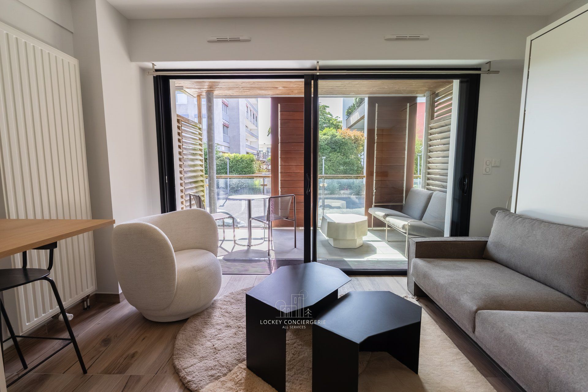 Un salon moderne comprenant un canapé, une table basse et un coin repas avec une table et des chaises. Une porte-fenêtre coulissante donne accès à un patio extérieur aménagé avec des sièges.