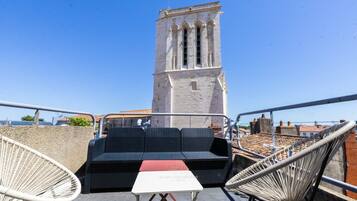 Una terrazza sul tetto con mobili in vimini, un tavolo e vista su una torre storica.