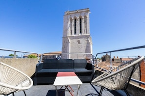 Una terrazza sul tetto con mobili in vimini, un tavolo e vista su una torre storica.