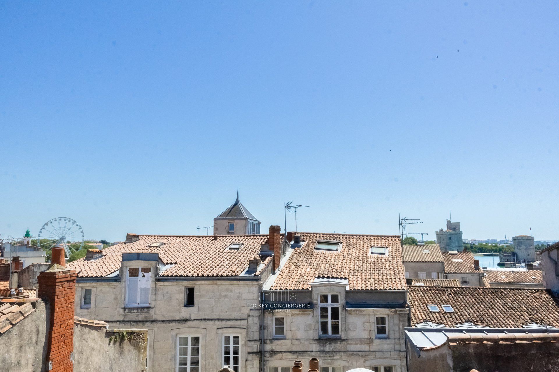 Un edificio con tetto in tegole, una piccola torre e un cartello che indica 'Lockey Conciergerie All Services'.