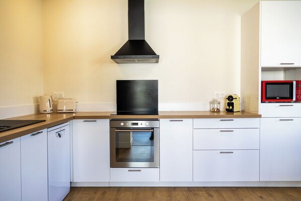 Una cocina moderna con armarios blancos, horno de acero inoxidable, campana extractora negra y microondas rojo.
