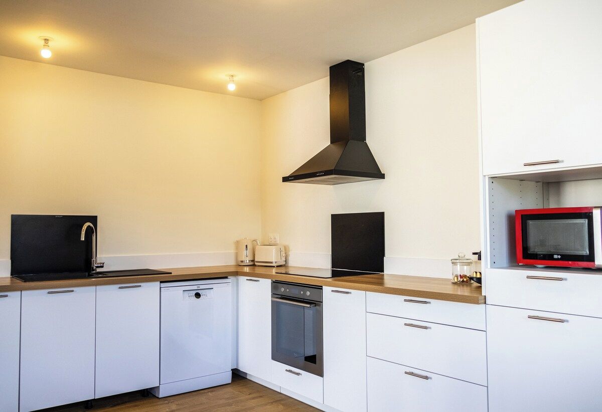A modern kitchen with white cabinetry, a black range hood, a microwave, and a dishwasher.