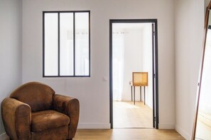 Una habitación con un sillón de cuero marrón, una ventana con persianas y una puerta que da a otra estancia.