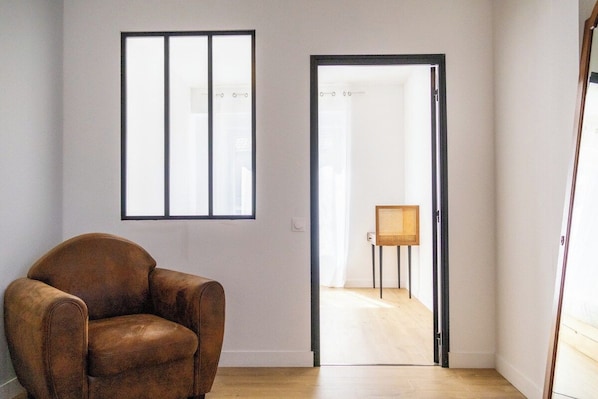 Een kamer met een bruine leren fauteuil, een raam met jaloezieën en een deur naar een andere kamer.