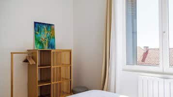 Een kamer met een bed, een houten kledingkast, een schilderij en een raam met gordijnen.