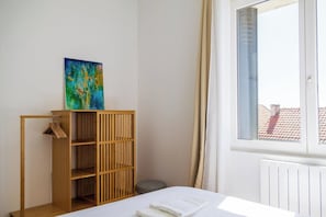 Een kamer met een bed, een houten kledingkast, een schilderij en een raam met gordijnen.